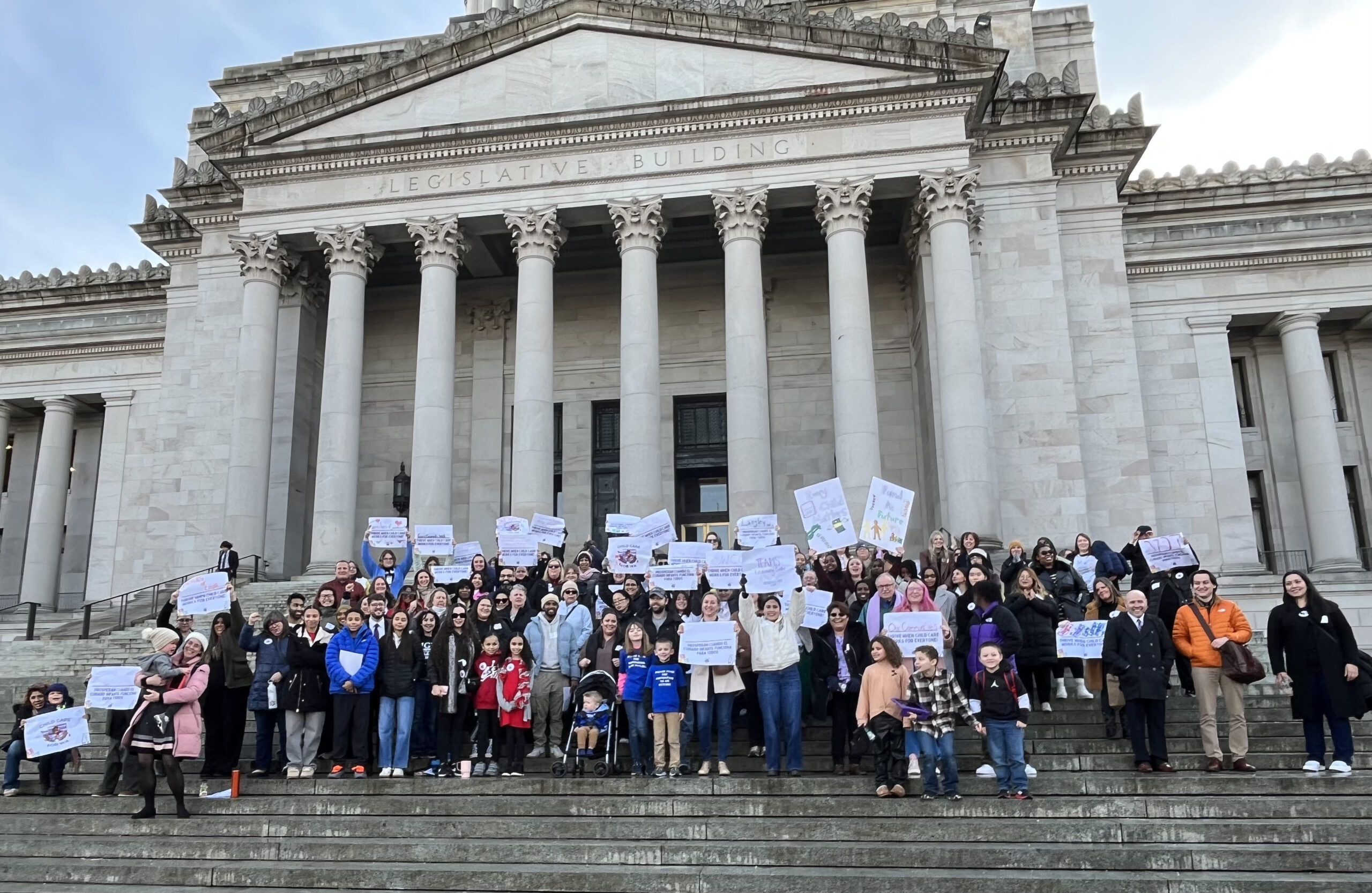A large group of people standing outside the Washington capitol building, holding signs with messages in support of child care